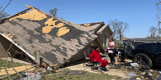 People sit in front of a damaged home on Saturday in Silver City, Miss. At least 25 people were killed in the state after a tornado ripped through several towns.