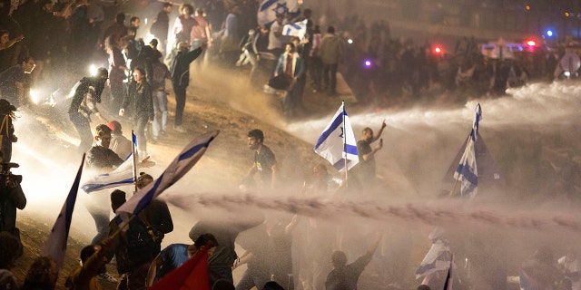 Israeli police use a water cannon to disperse demonstrators blocking a highway during a protest against plans by Prime Minister Benjamin Netanyahu's government to overhaul the judicial system in Tel Aviv, Israel, Monday, March 27, 2023. Tens of thousands of Israelis have poured into the streets across the country in a spontaneous outburst of anger after Prime Minister Benjamin Netanyahu abruptly fired his defense minister for challenging the Israeli leader's judicial overhaul plan.