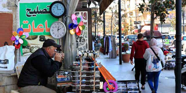 Un vendedor ambulante libanés que vende y repara relojes, se sienta junto a dos relojes que muestran diferentes horas en el Líbano, el 27 de marzo de 2023. El primer ministro interino del Líbano revierte la decisión de retrasar el inicio del horario de verano en un mes.