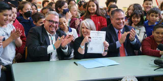 Gov. Michelle Lujan Grisham, center, holds a bill she signed during a celebration with sponsors Sens. Michael Padilla, right, and Leo Jaramillo, left, at Pinon Elementary School in Santa Fe, New Mexico, on March 27, 2023. The legislation provides universal free school meals for New Mexico students.