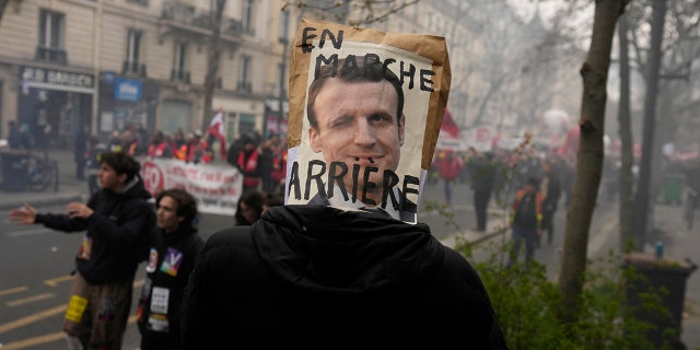 A demonstrator has a poster mocking French President Emmanuel Macron over his head during a demonstration March 28, 2023, in Paris.