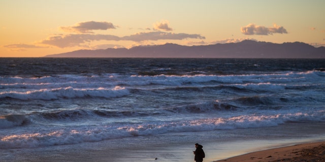 A lone person stands on the shore near the Manhattan Beach Pier, in Manhattan Beach, California, March 1, 2023. 