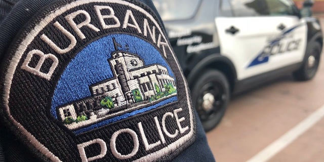 A Burbank, California police officer stands behind a Burbank police cruiser.