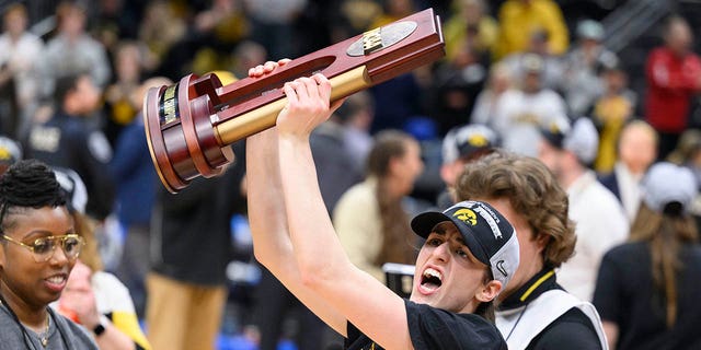 Iowa guard Caitlin Clark shows off the trophy as she celebrates after an Elite 8 college basketball game of the NCAA Tournament against Louisville, Sunday, March 26, 2023, in Seattle.