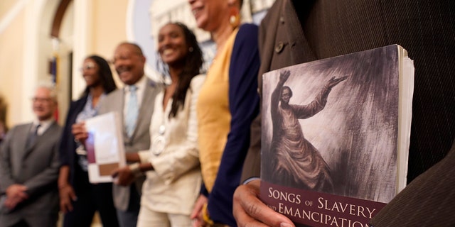 FILE — Dr.  Amos C. Brown, Jr., vice chair for the California Reparations Task Force, right, holds a copy of the book Songs of Slavery and Emancipation, as he and other members of the task force pose for photos at the Capitol in Sacramento, Calif., on June 16, 2022.