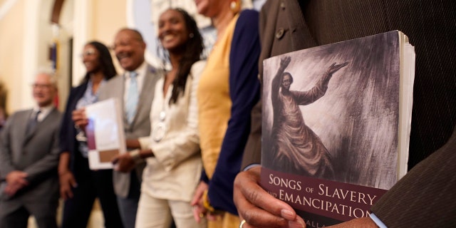 FILE — Dr. Amos C. Brown, Jr., vice chair for the California Reparations Task Force, right, holds a copy of the book Songs of Slavery and Emancipation, as he and other members of the task force pose for photos at the Capitol in Sacramento, Calif., on June 16, 2022.