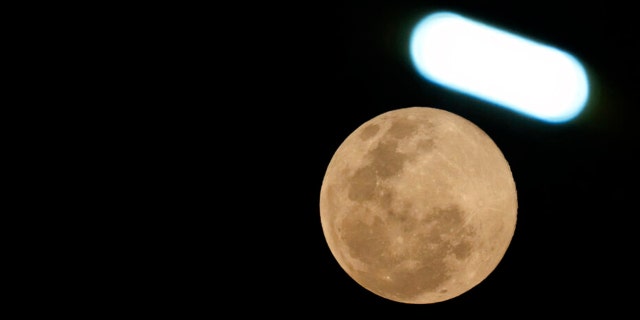 The moon shines under a street lamp in Phnom Penh Cambodia, Tuesday, March 7, 2023.