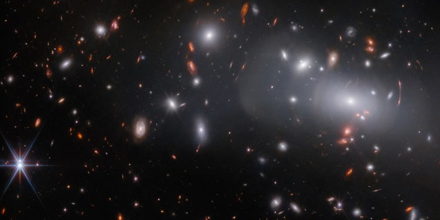 This observation from the NASA/ESA/Canadian Space Agency's James Webb Space Telescope features the massive galaxy cluster RX J2129.  Due to gravitational lensing, this observation contains three different images of the same supernova host galaxy, which you can see in closer detail here.  Gravitational lensing occurs when a massive celestial body causes enough curvature of space-time to bend the path of light passing through or through it, almost like a wide lens.  Gravitational reversal can cause background objects to appear oddly distorted, as can be seen by the concentric arcs of light in the upper right of this image.