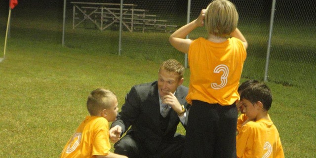 Daniel Prial is shown coaching a boys soccer team in Alabama while wearing a suit.