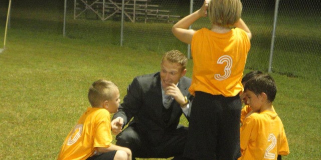 Daniel Prial is shown coaching a boys soccer team in Alabama while wearing a suit.