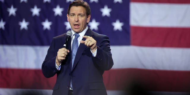 Ron DeSantis holding microphone, US flag behind him