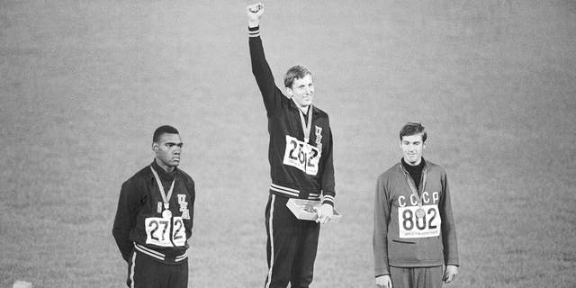 ARCHIVO - El medallista de oro Dick Fosbury levanta el brazo en el podio de ganadores en el Estadio Olímpico, el 20 de octubre de 1968, en la Ciudad de México.