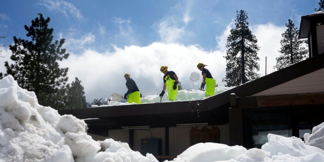 Members of a Cal Fire crew clear snow off the roof of the town's post office after a series of storms, Wednesday, March 8, 2023, in Crestline, California.