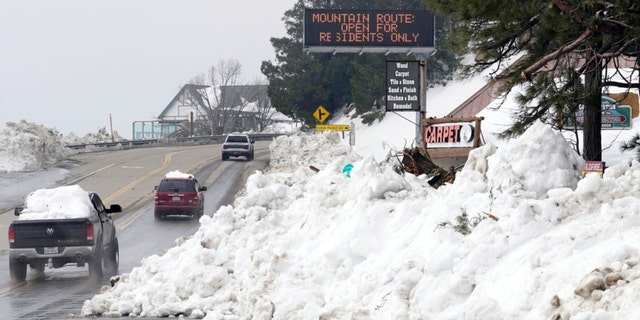Mounds of snow cover the sides of the main road leading out of the mountains after a series of storms Wednesday, March 8, 2023, in Lake Arrowhead. Californians are still struggling to dig out and get necessities in the aftermath of a record-setting blizzard last month.