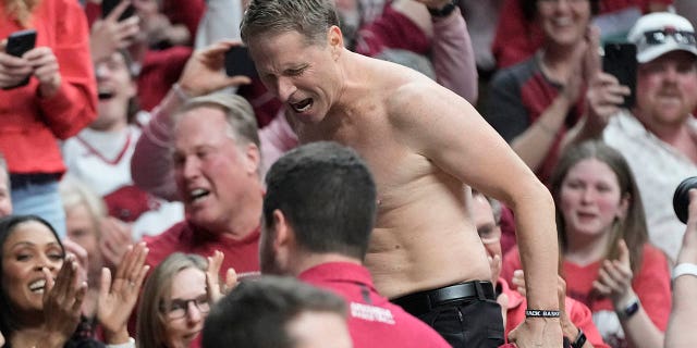Arkansas head coach Eric Musselman reacts on the press table with his shirt off.