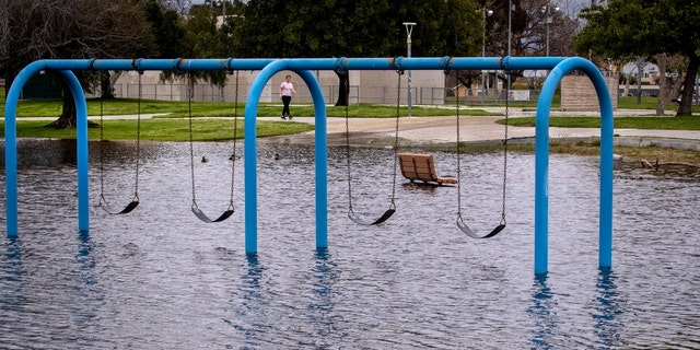 A person walks past a flooded playground section of the park including the swings, bench and open play area at Edison Community Park as a series of storms is hitting the Southland, with rain expected to intensify Tuesday and Wednesday in Huntington Beach Monday, March 20, 2023. 
