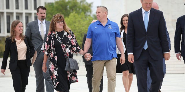 El ex entrenador asistente de fútbol americano de Bremerton High School, Joe Kennedy, sostiene la mano de su esposa Denise mientras camina por la Corte Suprema de los Estados Unidos con miembros de su equipo legal después de que su caso, Kennedy v. el distrito escolar de Bremerton, fuera discutido en la Corte Suprema el 25 de abril  , 2022 en Washington, DC.