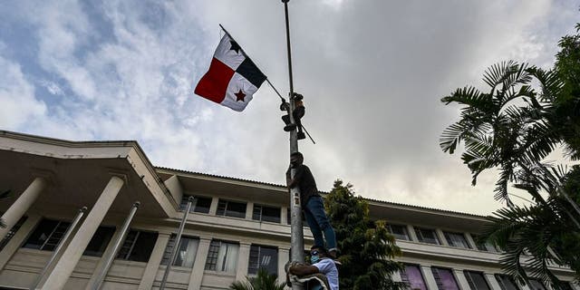 Men climb a light pole with a Panamanian flag during a protest against same-sex marriage, outside the Supreme Court of Justice, in Panama City on October 07, 2020. - Protesters asked Court magistrates supreme not to accept a denunciation of unconstitutionality against article 26 of the family code, which only recognizes the union between a man and a woman.
