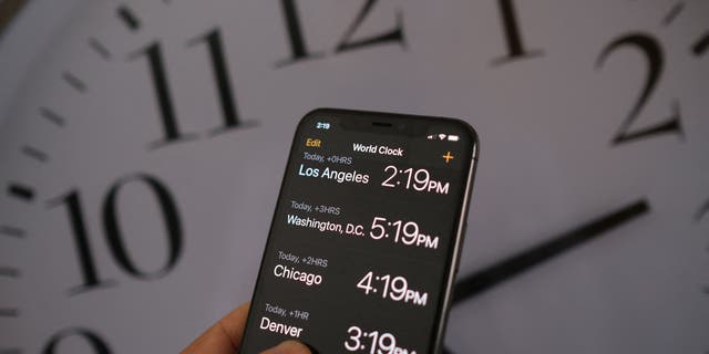 This illustration photo shows a clock in the background of a smartphone showing the time after daylight saving time was implemented in Los Angeles, California, on March 15, 2022. 