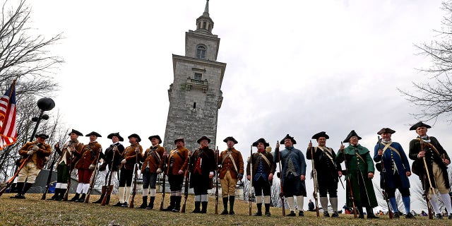 In a line, the Lexington Minutemen and a group of the Massachusetts Sons of American Revolution stand atop Dorchester Heights in Boston on March 17, 2022. The annual commemoration of Evacuation Day at Dorchester Heights in South Boston on Thursday, March 17, is hosted by the National Parks of Boston and South Boston Citizens Association.
