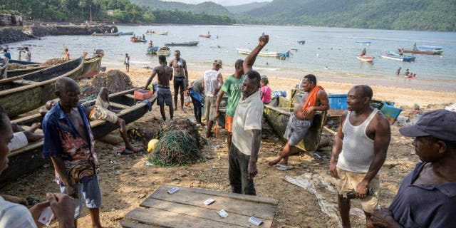 A group of men playing cards standing next to the fishing boats on the beach of Porto Alegre on Sao Tome Island in the Gulf of Guinea Feb 8, 2022.