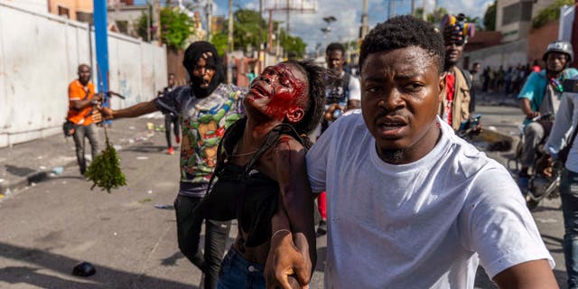 A man assists an injured woman during a protest against Haitian Prime Minister Ariel Henry, calling for his resignation, in Port-au-Prince, Haiti, October 10, 2022.