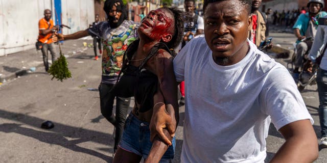 A man assists an injured woman during a protest against Haitian Prime Minister Ariel Henry, calling for his resignation, in Port-au-Prince, Haiti, October 10, 2022.