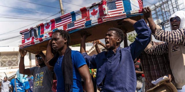 Demonstrators carry a coffin covered with American, Canadian and French flags and pictures of politicians as they protest on Jean-Jacques Dessalines Day in Port-au-Prince, Haiti, October 17, 2022.