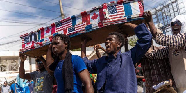 Demonstrators carry a casket covered with American, Canadian and French flags and pictures of politicians during a Jean-Jacques Dessalines Day protest in Port-au-Prince, Haiti, on October 17, 2022.