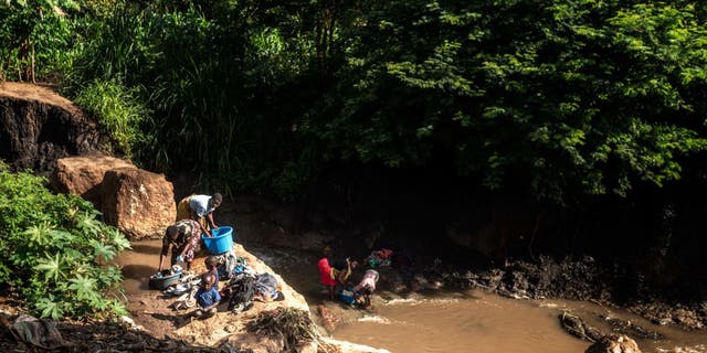 A group of women with their children wash clothes in a river that is contaminated in Lilongwe, Malawi, on Feb. 20, 2023.