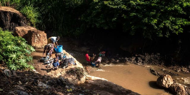 A group of women with their children wash clothes in a river that is contaminated in Lilongwe, Malawi, on Feb. 20, 2023.
