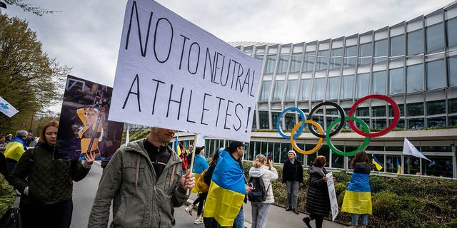 Ukrainians walk past the International Olympic Committee (IOC) headquarters during a protest against the IOC's proposed roadmap to organize the return of Russian athletes to competition under a neutral flag, provided they have "did not actively support the war in Ukraine" in Lausanne on March 25, 2023. 