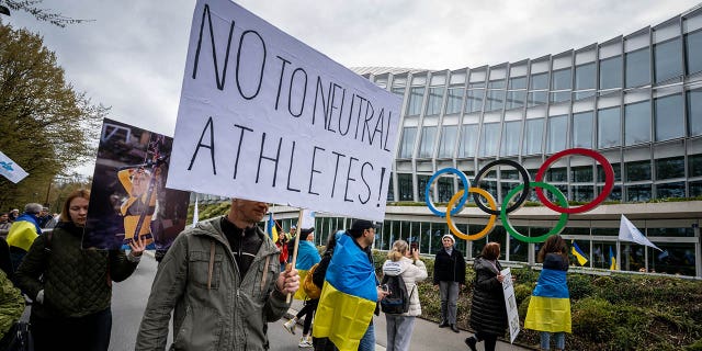 Ukrainians walk past the International Olympic Committee (IOC) headquarters during a protest against the IOC's proposed roadmap to organize the return of Russian athletes to competition under a neutral flag, provided they have "did not actively support the war in Ukraine" in Lausanne on March 25, 2023. 