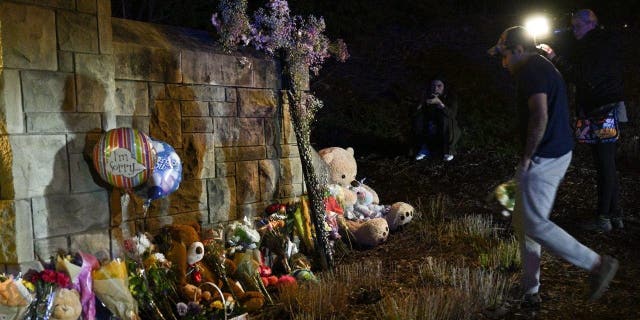 A man drops flowers to a makeshift memorial where balloons and teddy bears are left on the outside the Covenant School building at the Covenant Presbyterian Church, in Nashville, Tennessee, March 27, 2023.