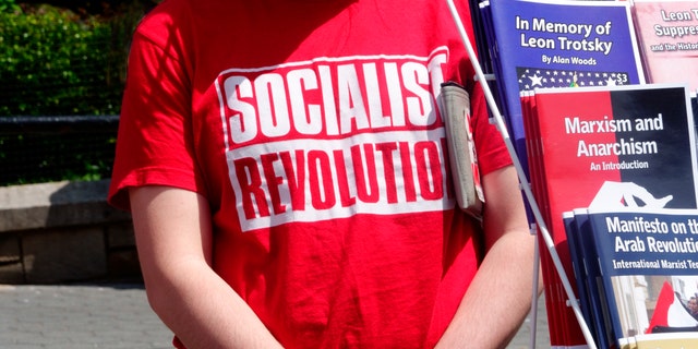 A socialist stands beside a group of pamphlets.