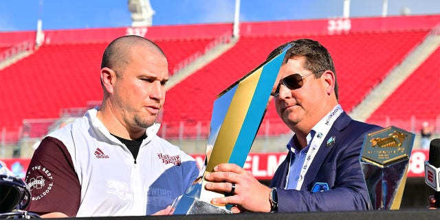 El CEO de ReliaQuest, Brian Murphy, a la derecha, entrega el trofeo al entrenador en jefe de los Mississippi State Bulldogs, Zach Arnett, después de derrotar a Illinois Fighting Illini 19-10 en el ReliaQuest Bowl en el Estadio Raymond James el 2 de enero de 2023 en Tampa, Florida.