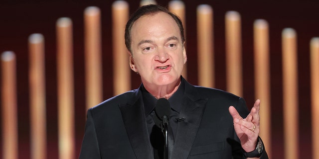 Quentin Tarantino speaks into a microphone at the Golden Globes, wearing an all-black suit