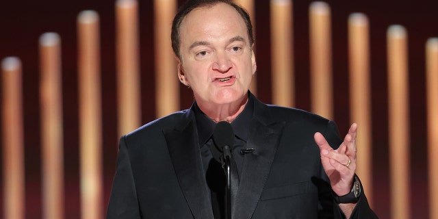 Quentin Tarantino speaks into a microphone at the Golden Globes, wearing an all-black suit