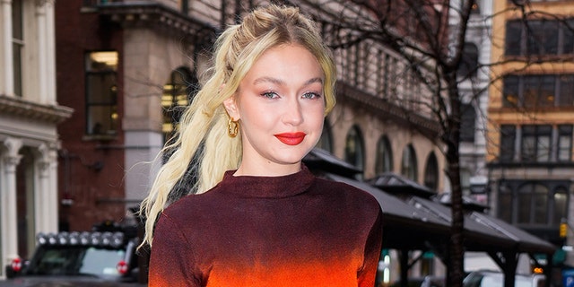 Gigi Hadid smiles for the camera while walking in New York City in an ombré maroon and red dress.