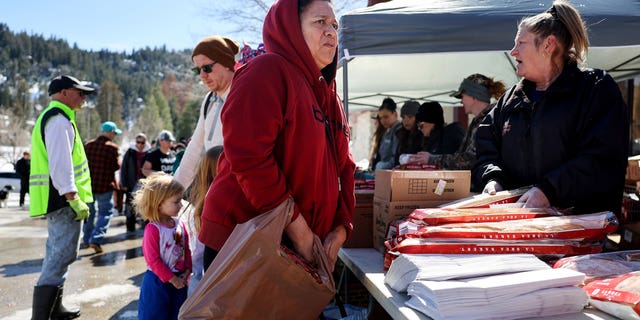 Longtime resident Dominga Mijangos receives donated food outside the local grocery store, which was severely damaged when its roof collapsed under the weight of several feet of snow, after a series of winter storms in the San Bernardino Mountains in Southern California on March 3, 2023 in Crestline, California.