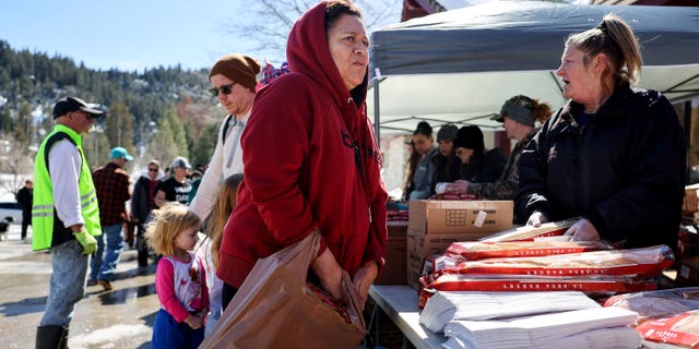 Longtime resident Dominga Mijangos receives donated food outside the local grocery store, which was severely damaged when its roof collapsed under the weight of several feet of snow, after a series of winter storms in the San Bernardino Mountains in Southern California on March 3, 2023 in Crestline, California.