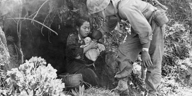 Okinawa, Japan: Eleven Okinawa civilians who were huddled in this hillside cave were rescued when a passing Marine patrol heard a baby crying. After they were assured that no harm would come to them, they emerged from their hideout; here, a leatherneck lends a hand to a mother and baby. 