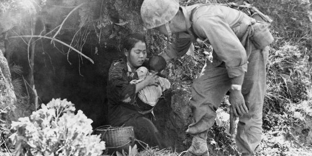 Okinawa, Japan: Eleven Okinawa civilians who were huddled in this hillside cave were rescued when a passing Marine patrol heard a baby crying. After they were assured that no harm would come to them, they emerged from their hideout; here, a leatherneck lends a hand to a mother and baby.