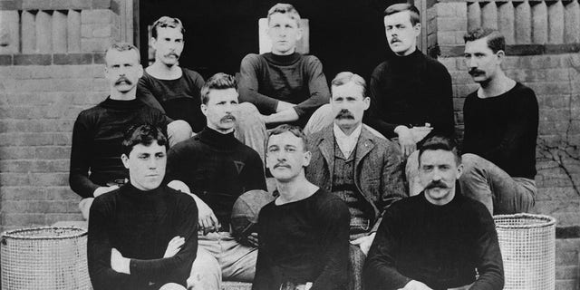 The first basketball team, consisting of nine players and their coach on the steps of the Springfield College Gymnasium in 1891, are shown. Basketball inventor Dr. James Naismith is wearing vest and coat. Grouped with him are left to right, from back row: John G. Thompson, Eugene S. Libby, Edwin P. Ruggles, William R. Chase and T. Duncan Patton. In the center row are Frank Mahan and Dr. James Naismith. In the front row, Finlay G. MacDonald, William H. Davis and Lyman W. Archibald.