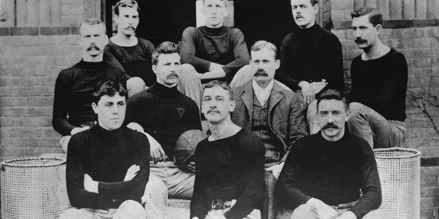 The first basketball team, consisting of nine players and their coach on the steps of the Springfield College Gymnasium in 1891, are shown. Basketball inventor Dr. James Naismith is wearing vest and coat. Grouped with him are left to right, from back row: John G. Thompson, Eugene S. Libby, Edwin P. Ruggles, William R. Chase and T. Duncan Patton. In the center row are Frank Mahan and Dr. James Naismith. In the front row, Finlay G. MacDonald, William H. Davis and Lyman W. Archibald.