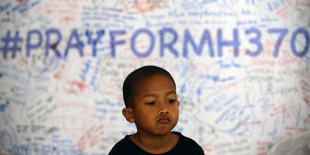 A young Malaysian child poses in front of a message board with well wishes to people involved with the missing Malaysia Airlines jetliner MH370, in Sepang, outside Kuala Lumpur, Malaysia, March 16, 2014. 