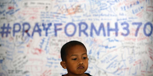 A young Malaysian child poses in front of a message board with well wishes to people involved with the missing Malaysia Airlines jetliner MH370, in Sepang, outside Kuala Lumpur, Malaysia, March 16, 2014. 