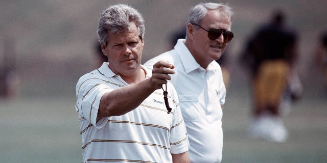 El director de personal de jugadores de los Pittsburgh Steelers, Dick Haley, a la izquierda, mira un cronómetro mientras cronometra a los jugadores en la carrera de 40 yardas mientras el entrenador en jefe Chuck Noll observa durante la práctica en el campo de entrenamiento de verano en St. Vincent College en julio de 1991 en Latrobe. Pensilvania. 