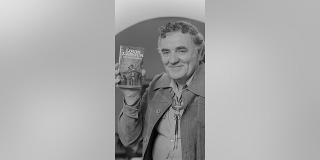 One of America's bestselling Western novelists, Louis L'Amour, is shown holding up his book "The Californians" at his home in California.  