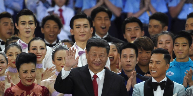China's President Xi Jinping (C) waves as he stands onstage with Hong Kong performer Lisa Wang (L) and actor Donnie Yen (R) as Xi joins performers at the end of a variety show in Hong Kong on June 30, 2017.
